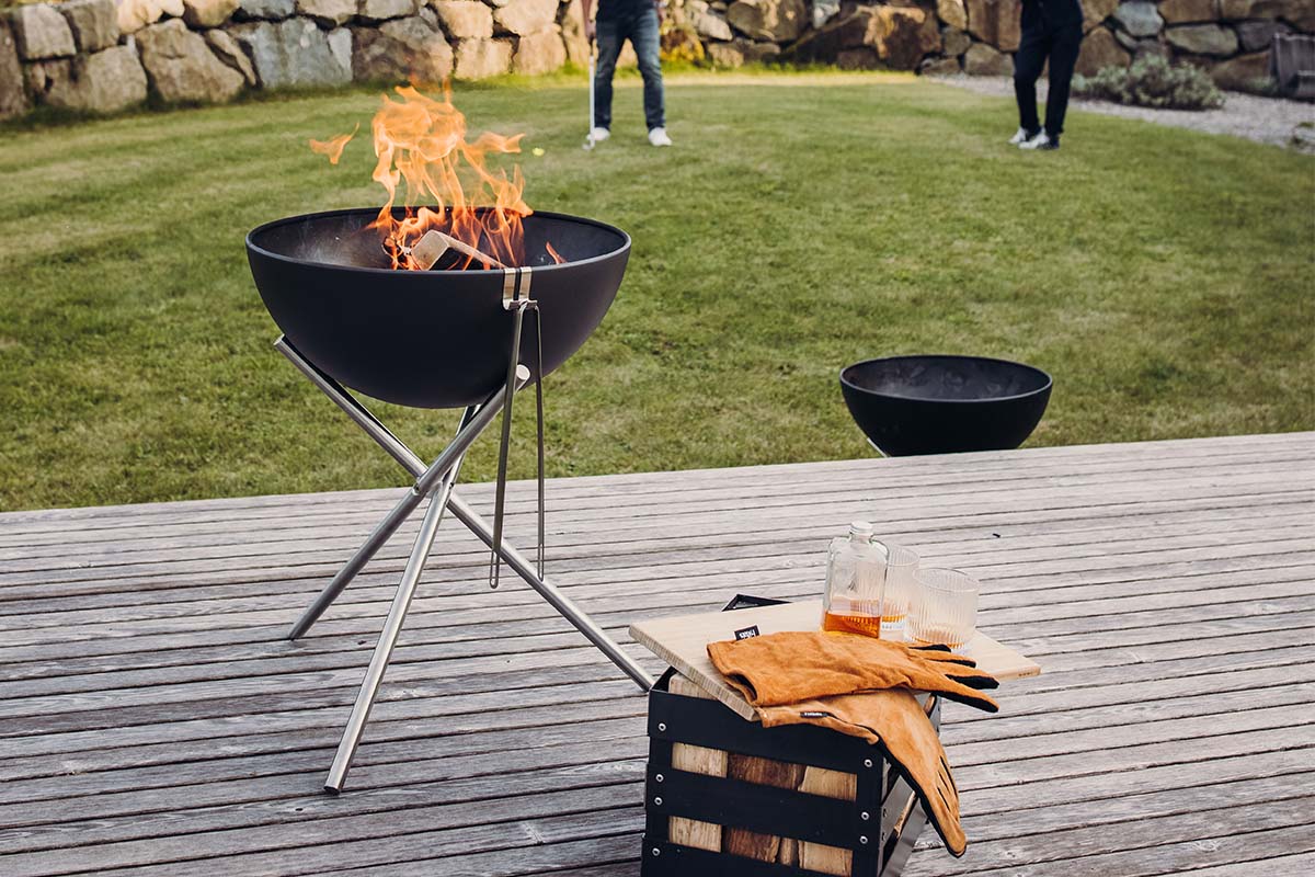 BOWL 57 Tripod A fire pit with a fire in it, with the 00342 Bowl 57 Tripod adding a functional and elegant touch to the scene.