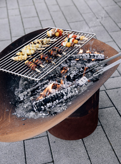 Illustrated is a grill with a lot of food on it, with the ELLIPSE Fire Bowl.