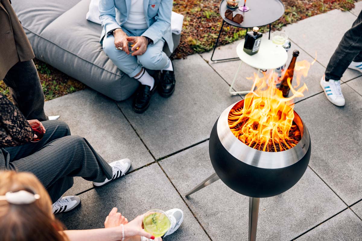 MOON 45 Fire basket with high stand A group of people sitting around a fire pit, with the 00717 Moon 45 with high stand adding a functional and elegant touch to the scene.