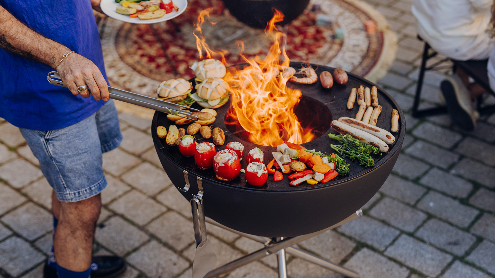 Scene waarin een man eten aan het koken is op een grill, waarbij de Bowl 70 BBQ Set opvalt door zijn praktische elegantie.