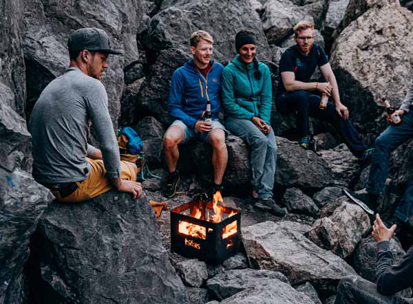 An image showing group of people sitting around a campfire, with the BEER BOX Fire Basket.