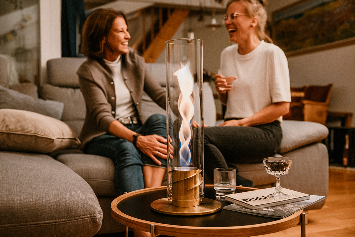 SPIN 1200 Tabletop Fireplace gold a woman sitting on a couch next to a Spin 1200 Tablefire Gold