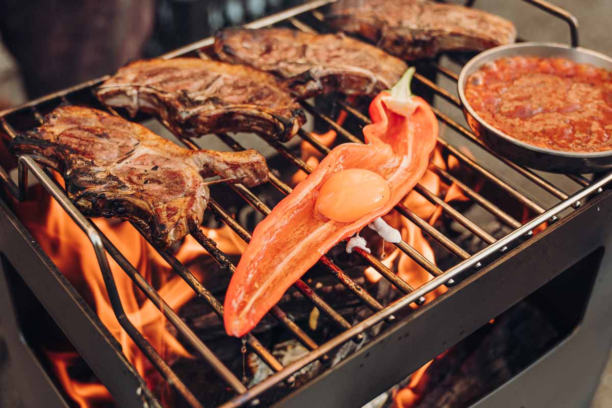 BEER BOX Fire Basket The Beer Box Firebasket is shown as a grill with meat and vegetables on it, creating a stylish and accessible visual.