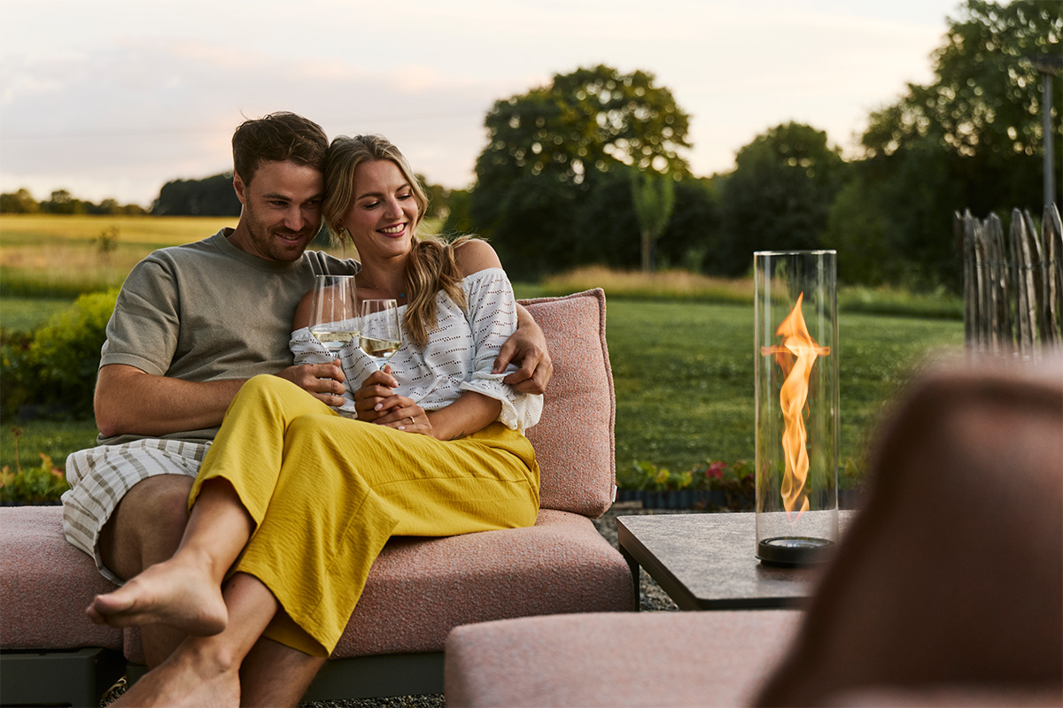 SPIN air 900 Einbau Ein Paar sitzt zusammen auf Gartencouch und schaut in die Flamme von SPIN air Einbau im Beistelltisch.
