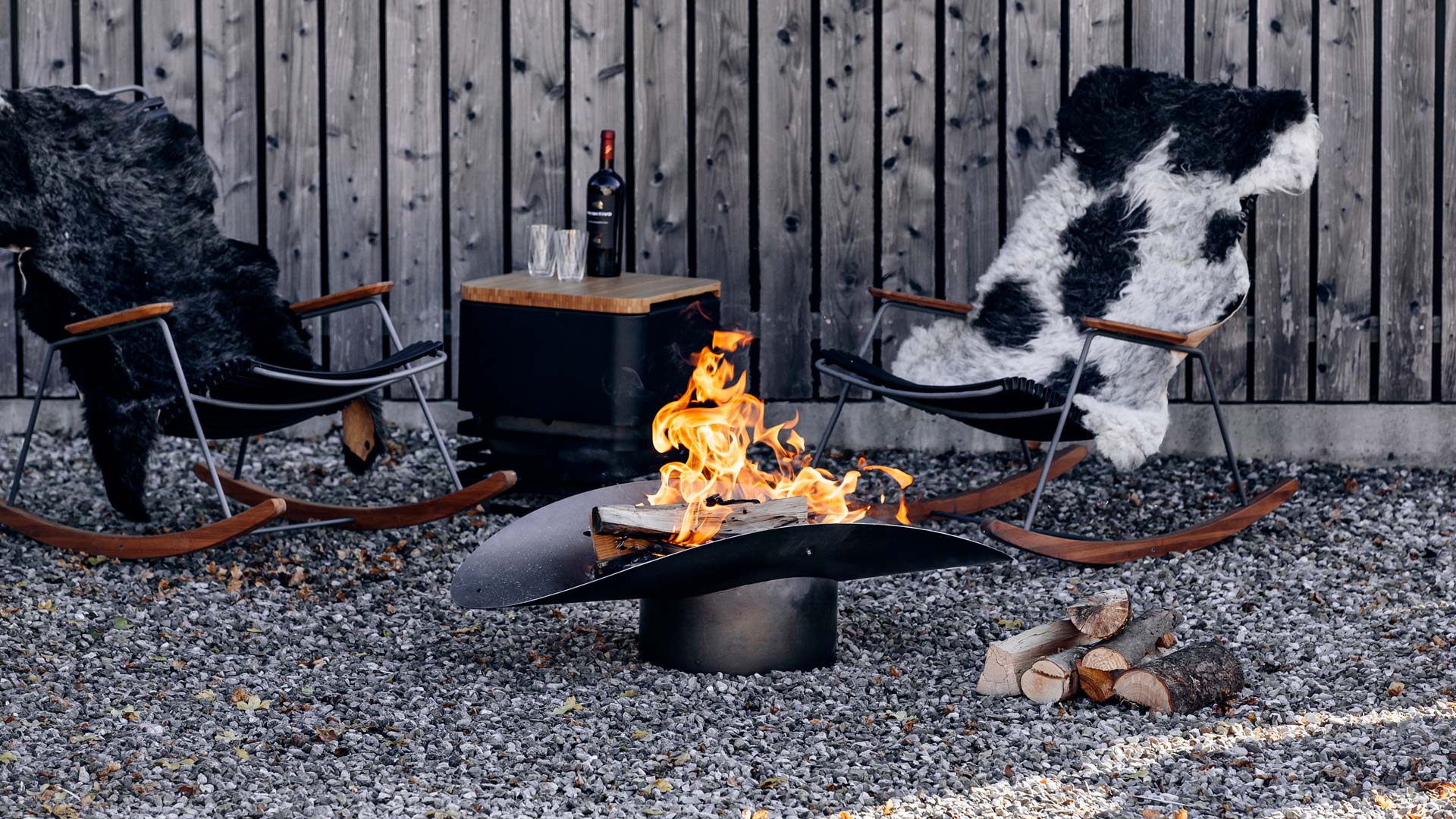 The photo presents two firebowls and a fire pit in the middle of a graveled area, with the ELLIPSE Fire Bowl.