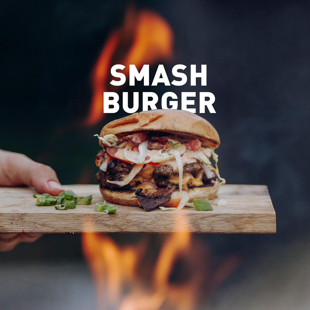 A view of a person holding a hamburger with a fire in the background