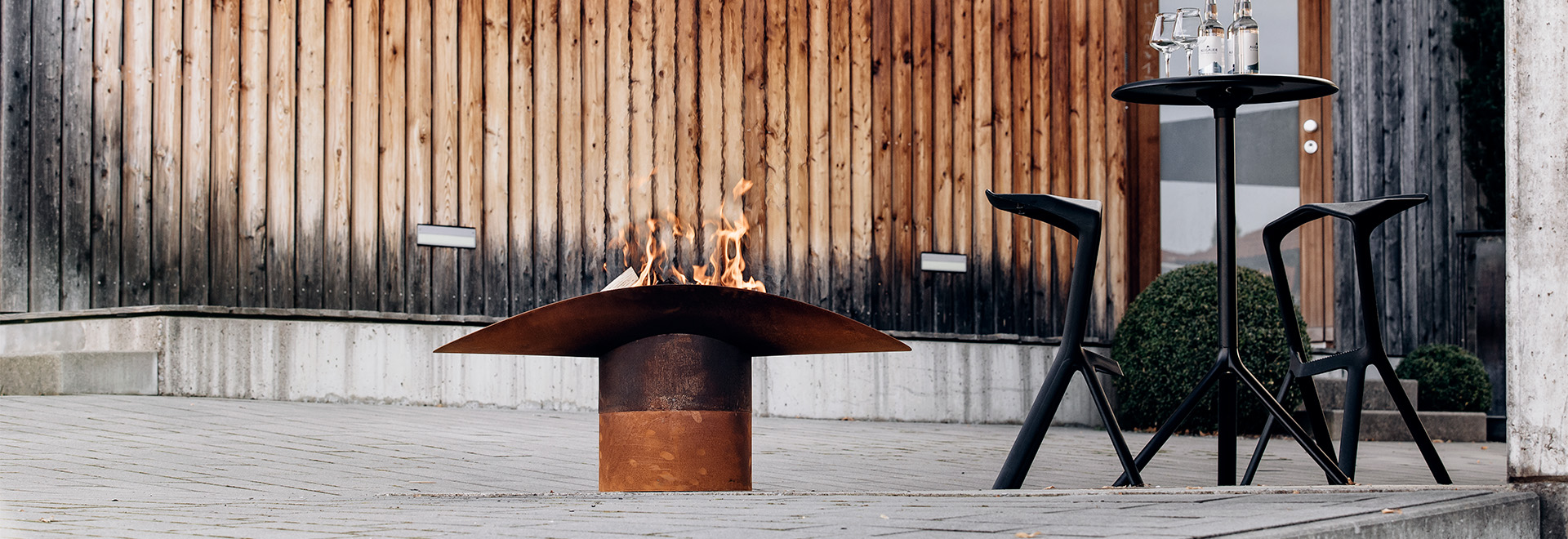 A view of a fire pit sitting on a sidewalk next to a building, with the ELLIPSE Fire Bowl.