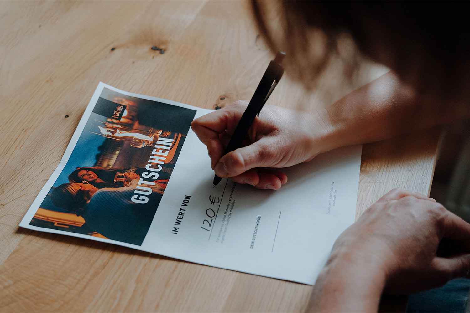 Digitale Geschenk-Gutscheine Ein Bild zeigt eine Person, die auf einem Stück Papier schreibt, mit dem digitalen GESCHENKGUTSCHEIN.