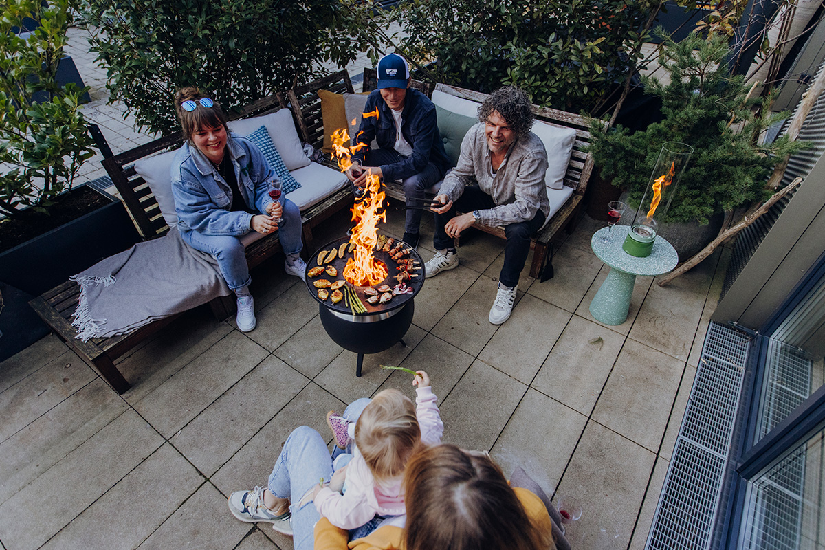 MOON 45 Plancha A depiction of a group of people sitting around a fire pit, featuring the 00861 Moon 45 Plancha Fireplace as a central and purposeful element.