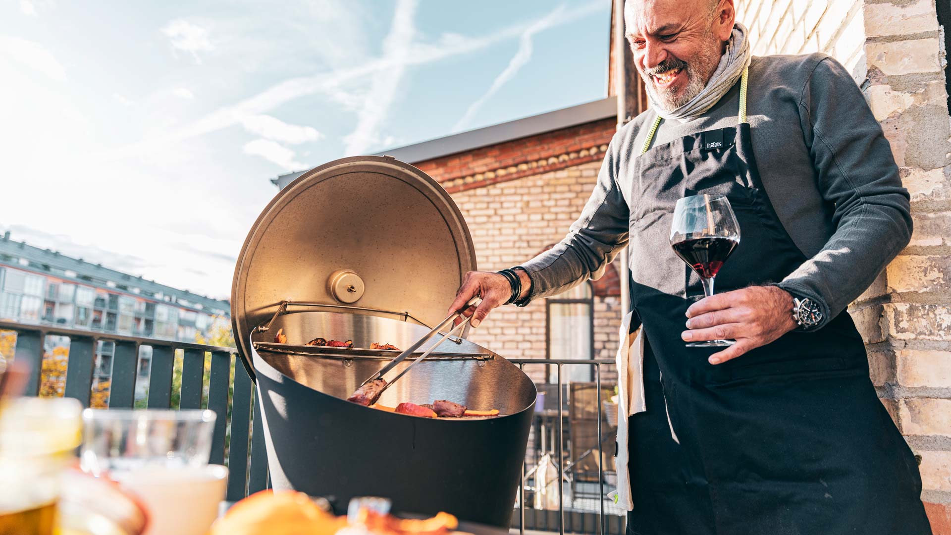 A view of a man cooking food on a grill outside, with the CONE Cover.
