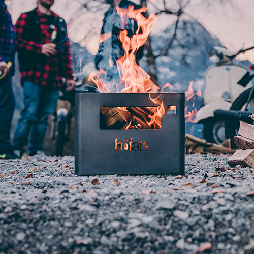 Hier ist ein Feuer mitten auf einem Feld dargestellt, mit dem LOGO BEER BOX Feuerkorb.