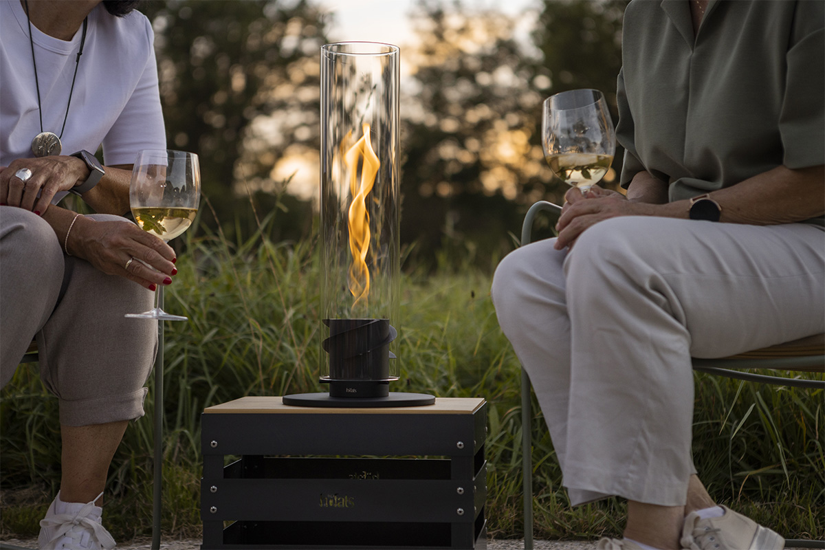 SPIN 1200 Tabletop Fireplace black An inviting scene with a man and woman sitting on a bench with wine glasses, highlighted by the presence of the 00700 Spin 1200 Tablefire black