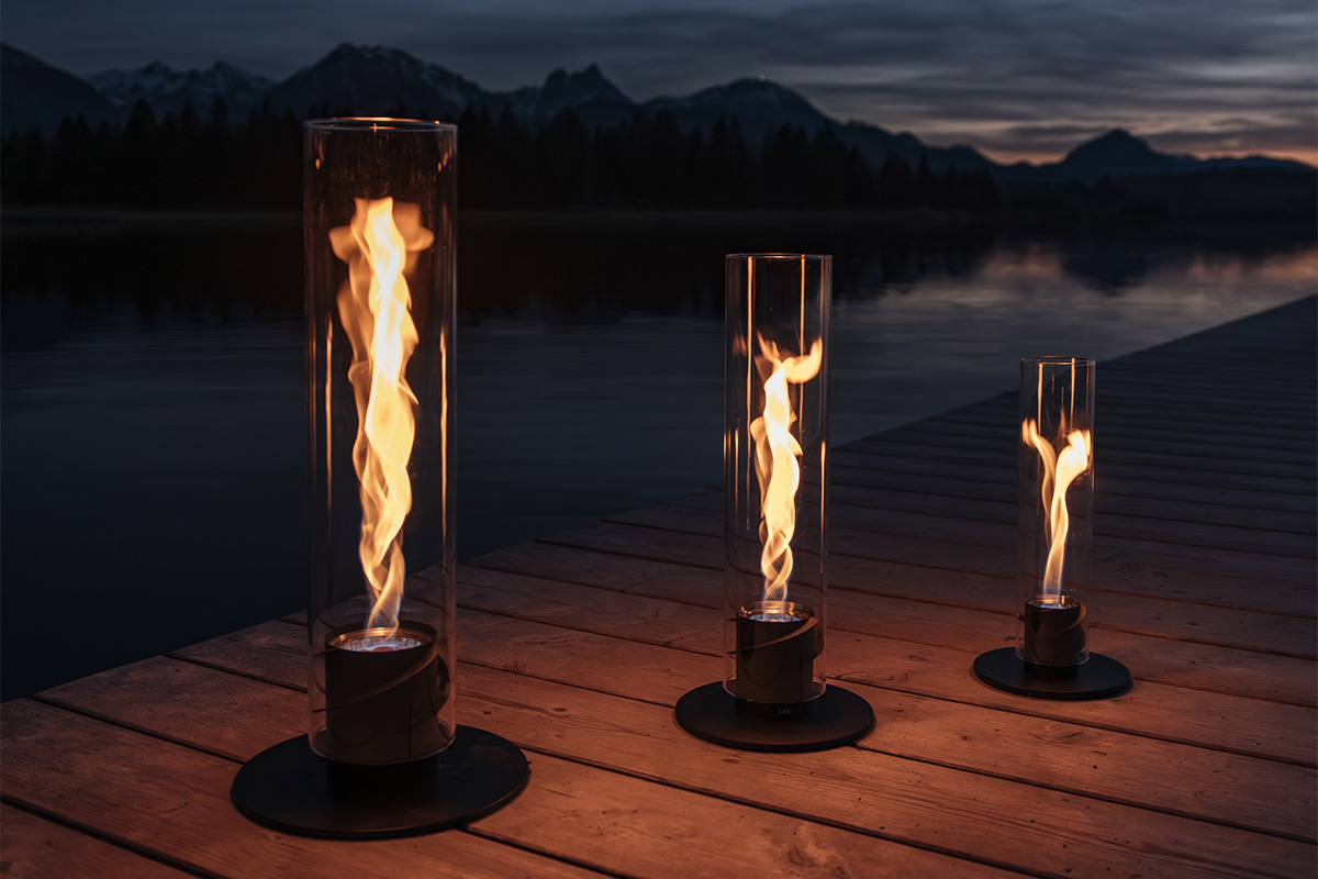 The 00628 Spin 1500 Tablefire black integrates seamlessly into the setting, where two torches on a dock with a lake in the background.