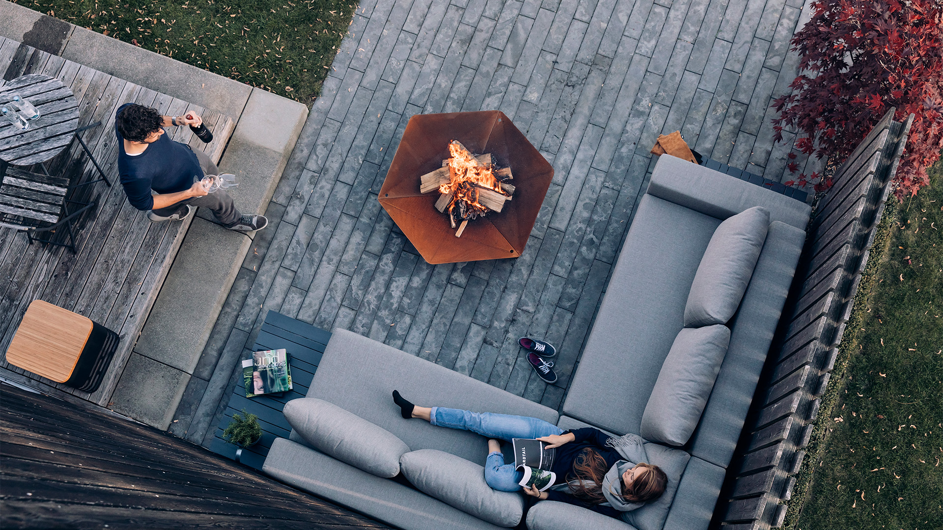 Scene showing a couple sitting on a couch in a backyard, where the Triple 120 Fireplace stands out for its practical elegance.