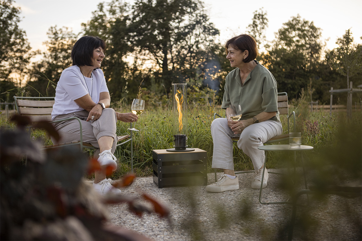 SPIN 1200 Tabletop Fireplace black The 00700 Spin 1200 Tablefire black integrates seamlessly into the setting, where two people sitting on a bench.