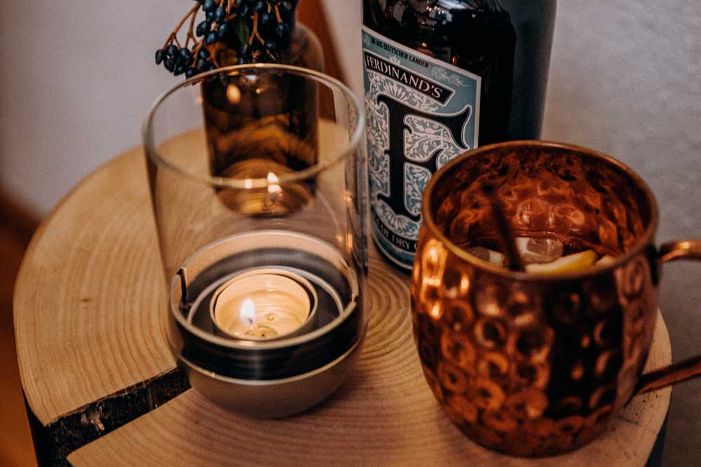 GRAVITY CANDLE Lantaarn zilver Een beeld van een kaars en een glas wijn op een tafel, met de LOGO GRAVITY CANDLE M90 lantaarn.