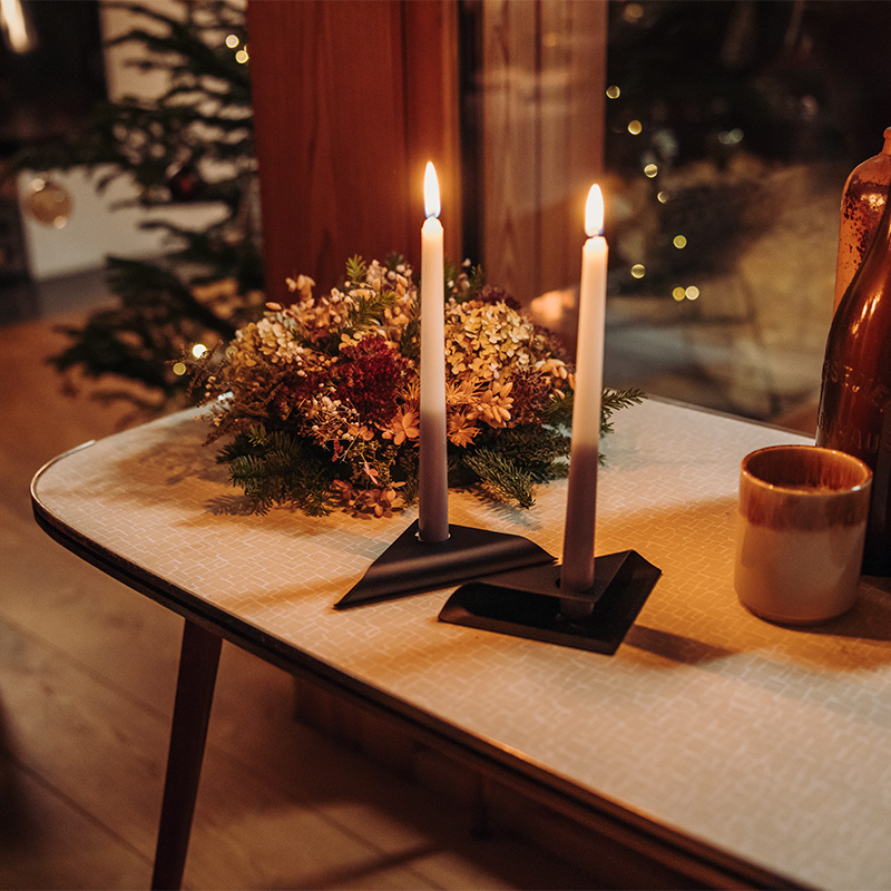 Scène waarbij een kaars en een vaas op een tafel staan, waarbij de Square Candle Candleholder opvalt door zijn praktische elegantie.