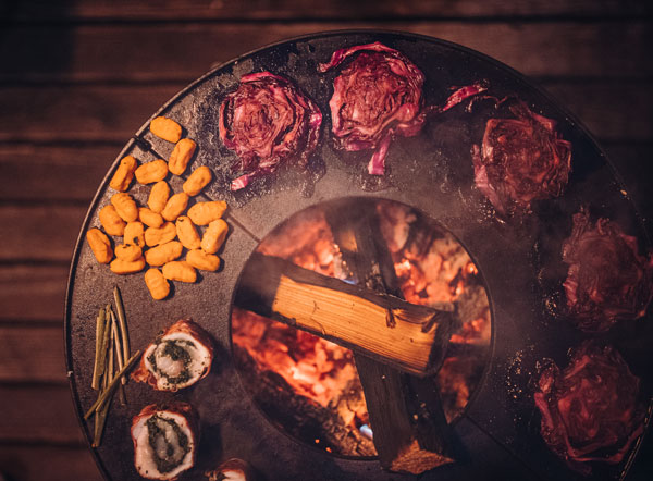 Dieses Bild zeigt einen Grill mit Fleisch und Gemüse darauf, zusammen mit der BOWL Feuerschale.