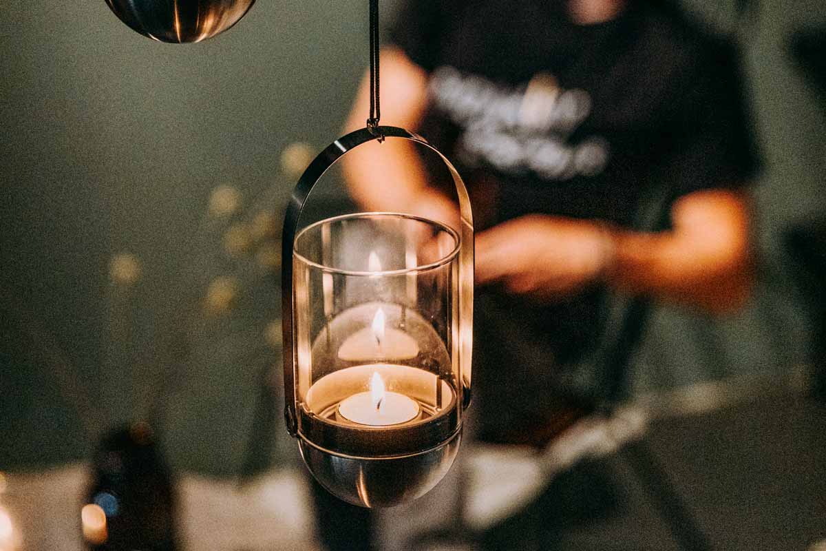 GRAVITY CANDLE Système de suspension Le système de suspension de bougie Gravity Candle s'intègre parfaitement dans le décor, où un homme se tient derrière une table avec une bougie.