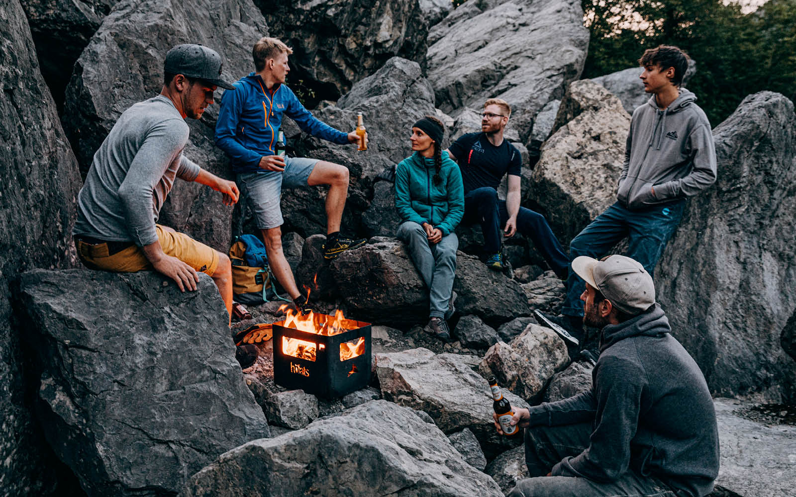 Abgebildet ist eine Gruppe von Menschen, die um ein Feuer sitzen, mit dem BEER BOX Feuerkorb.