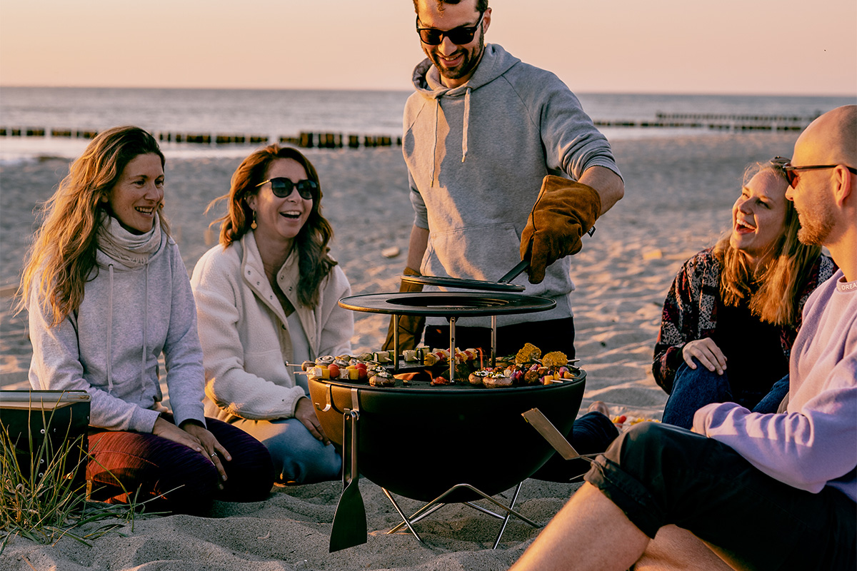BOWL 57 Sear Grate Illustrated is a group of people sitting on the beach, with the BOWL 57 Warming Ring.