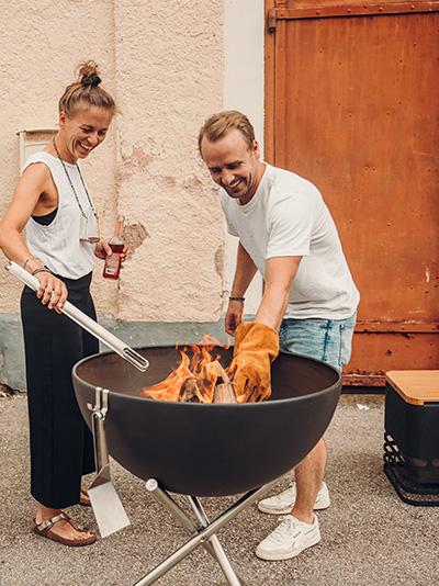 Un homme et une femme cuisinent sur un gril, enrichis par la présence des Firegloves, qui fusionnent design et utilité.