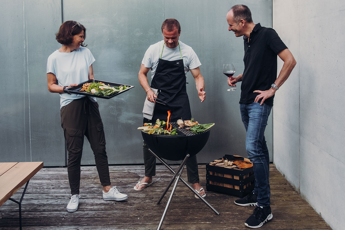 BOWL 57 Feuerset flex Auf dem Foto sind ein Mann und eine Frau beim Grillen mit dem BOWL 57 Fire Set flex zu sehen.
