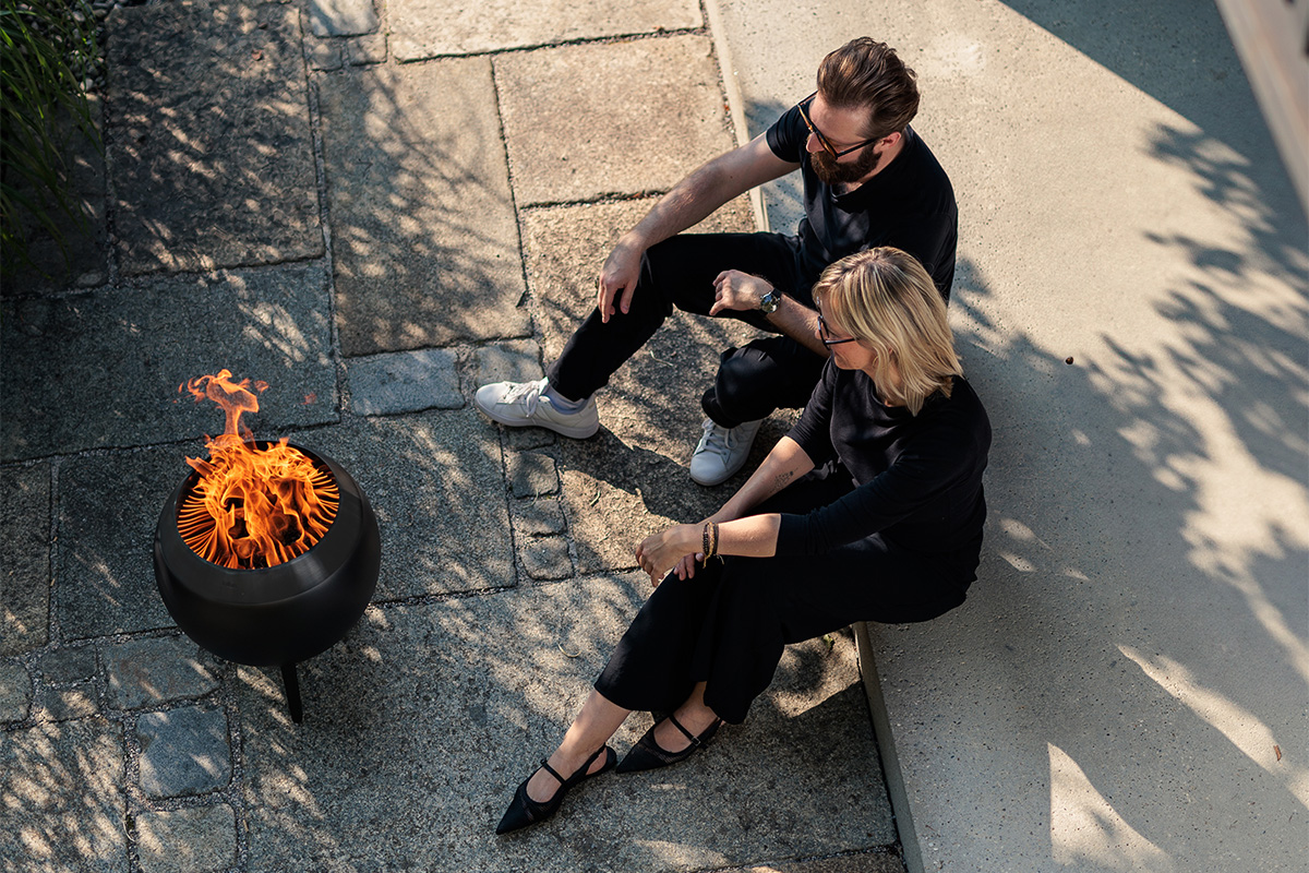 Bild aus der Vogelperspektive. Zwei Personen schauen auf einer Terrasse sitzend in die lodernde Flamme von MOON.