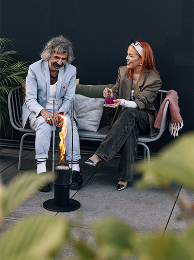 Eine Frau sitzt auf einer Bank und die Spin 1500 Pedestal Fireplace ergänzt den Moment mit ihrem durchdachten Design.