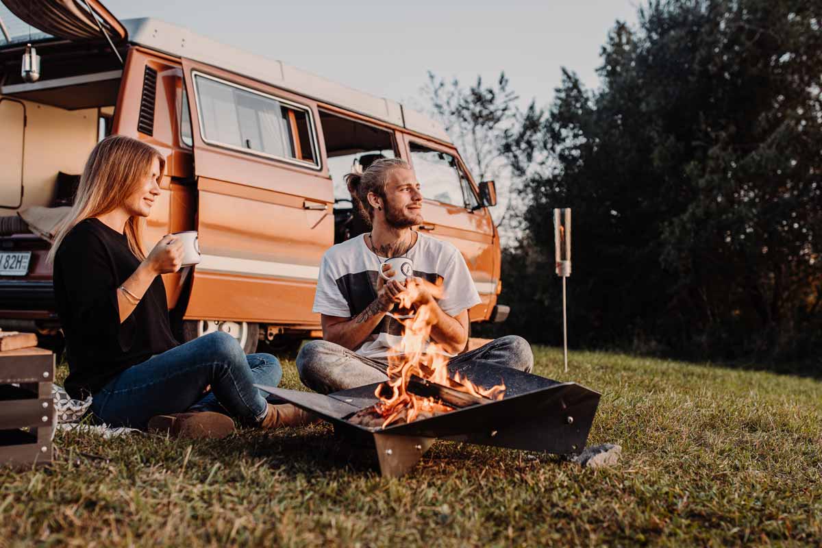 TRIPLE 90 Fire Bowl The photo presents a couple sitting on the grass next to a camper van, with the TRIPLE 90 Fire Bowl.