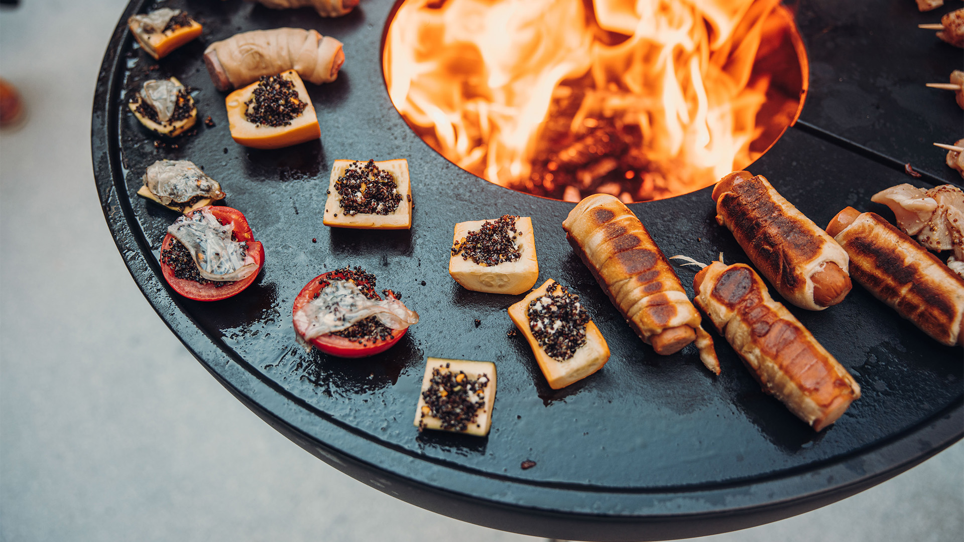 The 00263 Bowl 70 Plancha integrates seamlessly into the setting, where a fire pit with a bunch of meat on it.