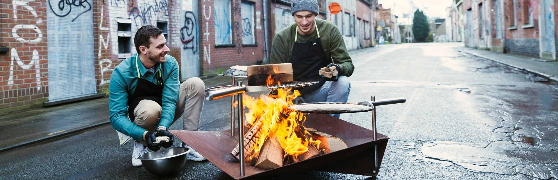 Dargestellt sind zwei Personen, die um eine Feuerstelle sitzen, mit dem Grillanzünder.