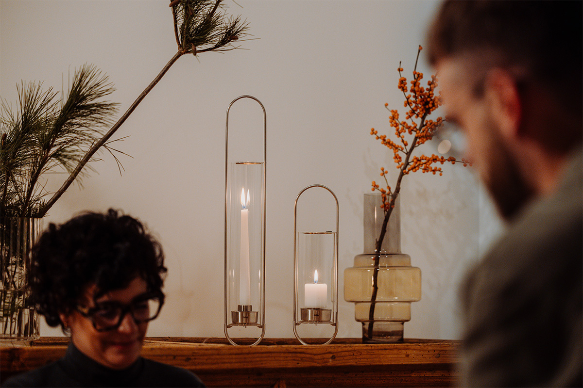 OVAL CANDLE 55 Bougeoir argent Une représentation d'un homme assis devant une table avec un vase et une bougie, mettant en vedette la OVAL CANDLE 55 comme élément central et utile.