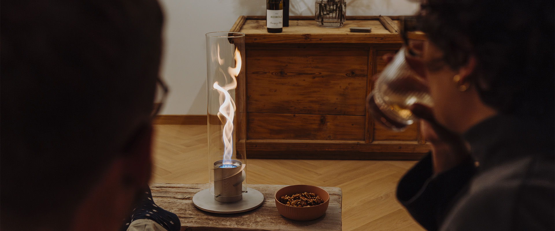 a man sitting on a wooden table with a glass of wine, shwing the Spin Tablefire in front of him creating a stylish and accessible visual.