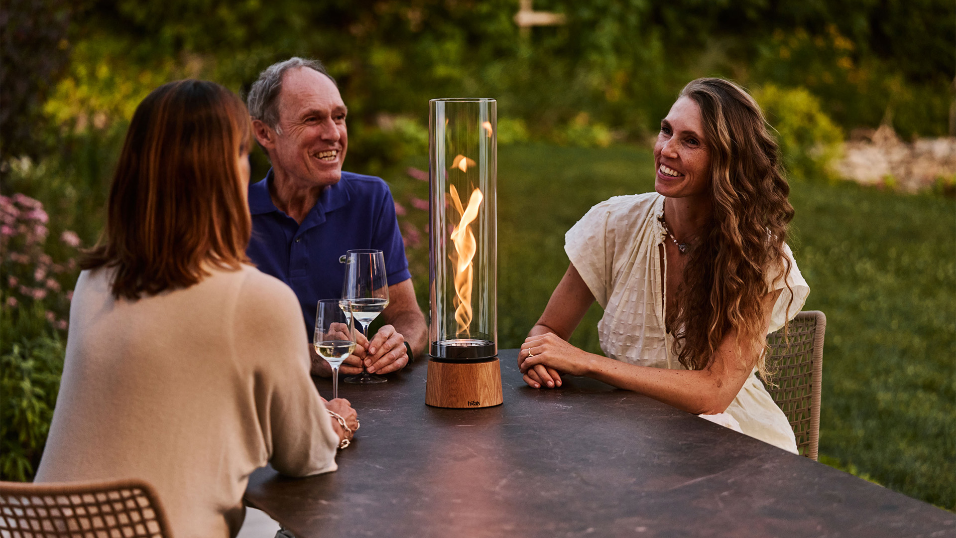 Drei Personen sitzen im Garten am Tisch und unterhalten sich. In der Mitte des Tisches brennt SPIN air Eiche.