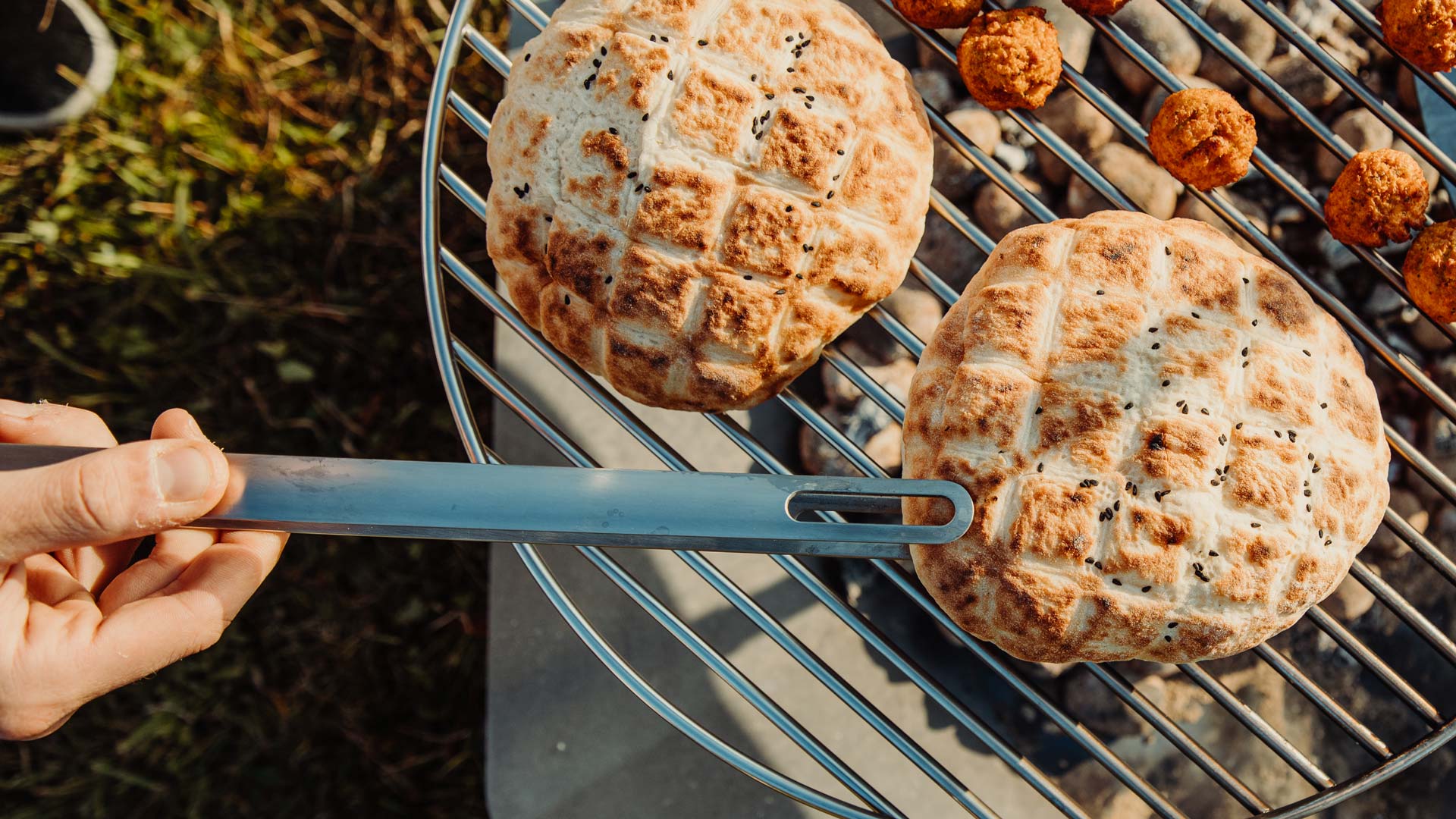 Een afbeelding van een persoon die voedsel aan het koken is op een grill, met het Triple 65 Fireplace BBQ Set als centraal en doelgericht element.