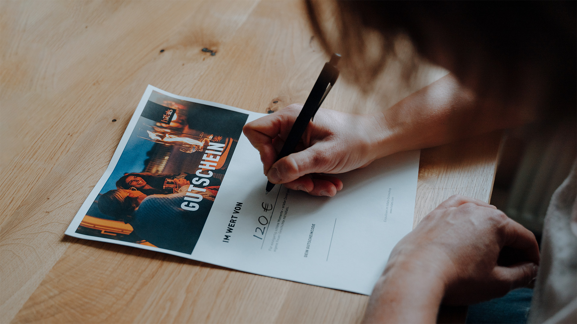 Dieses Bild zeigt eine Person, die auf einem Stück Papier schreibt, mit dem digitalen GESCHENKGUTSCHEIN.