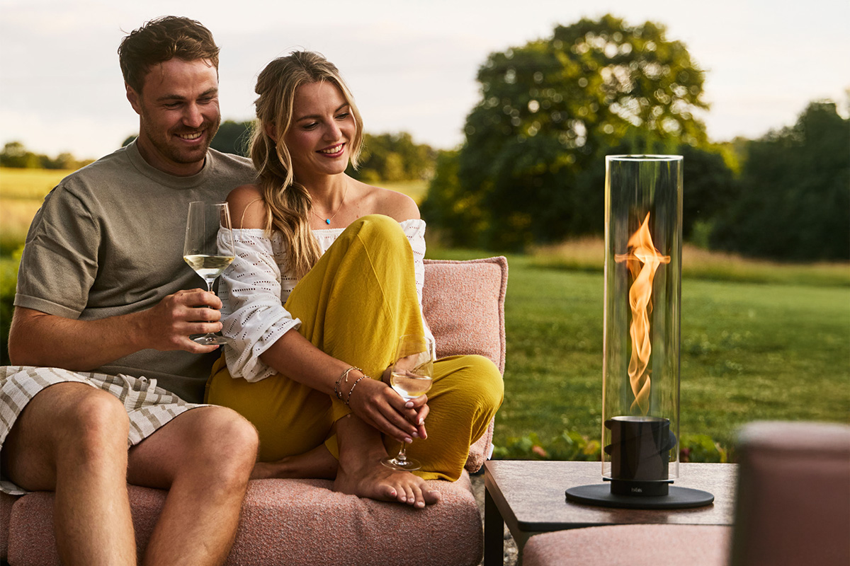 SPIN 1200 Tabletop Fireplace black Ein Paar sitzt zusammen auf Gartencouch und schaut in die Flamme von SPIN air Einbau im Beistelltisch.