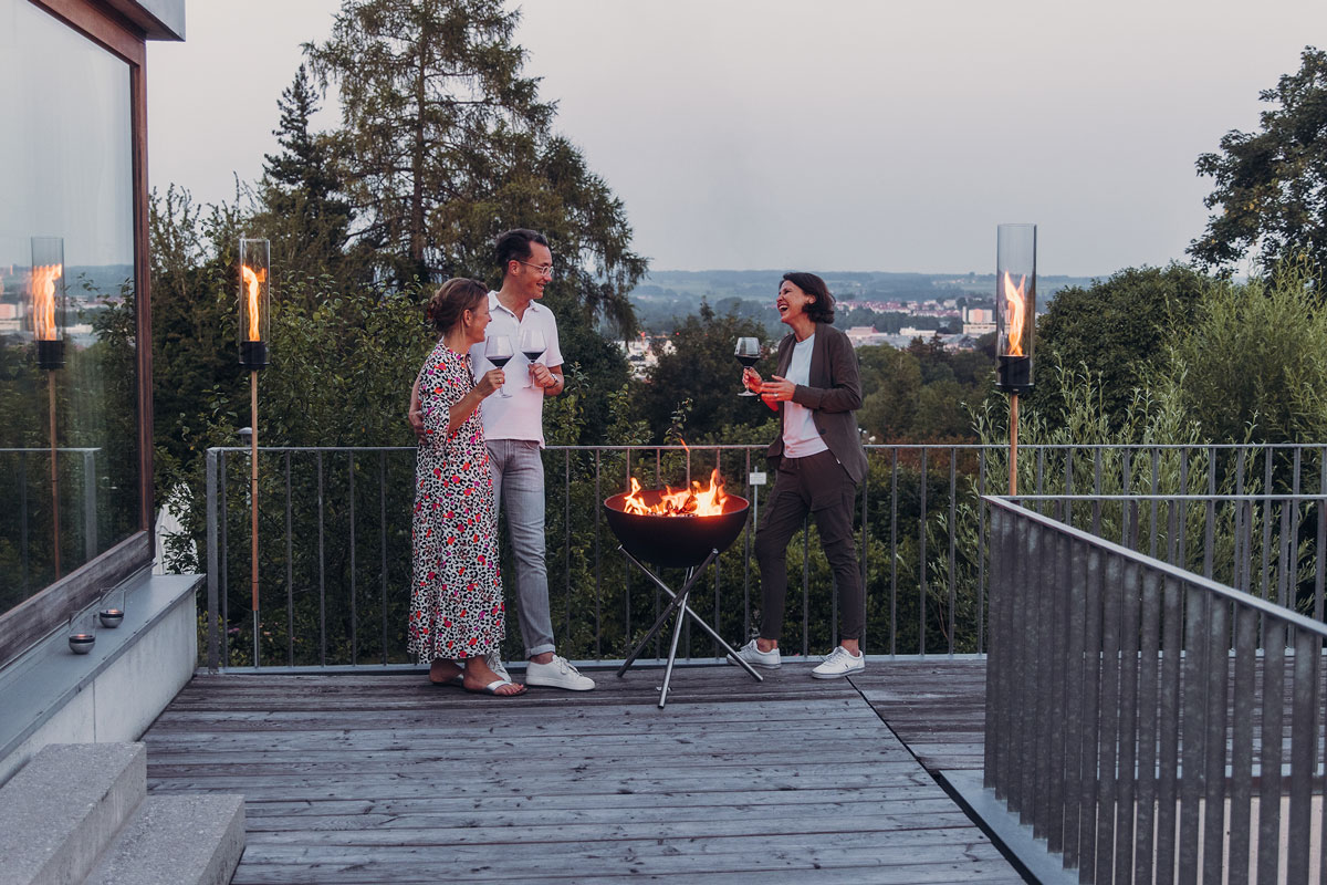 BOWL 57 Fire Bowl with tripod A man and woman standing on a deck with a fire, with the 00250 Bowl 57 with Tripod adding a functional and elegant touch to the scene.