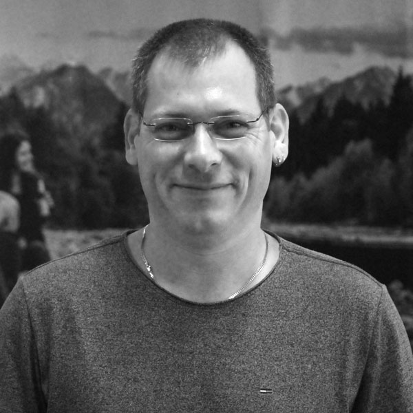 Ein Mann mit Brille steht vor einem Gemälde.