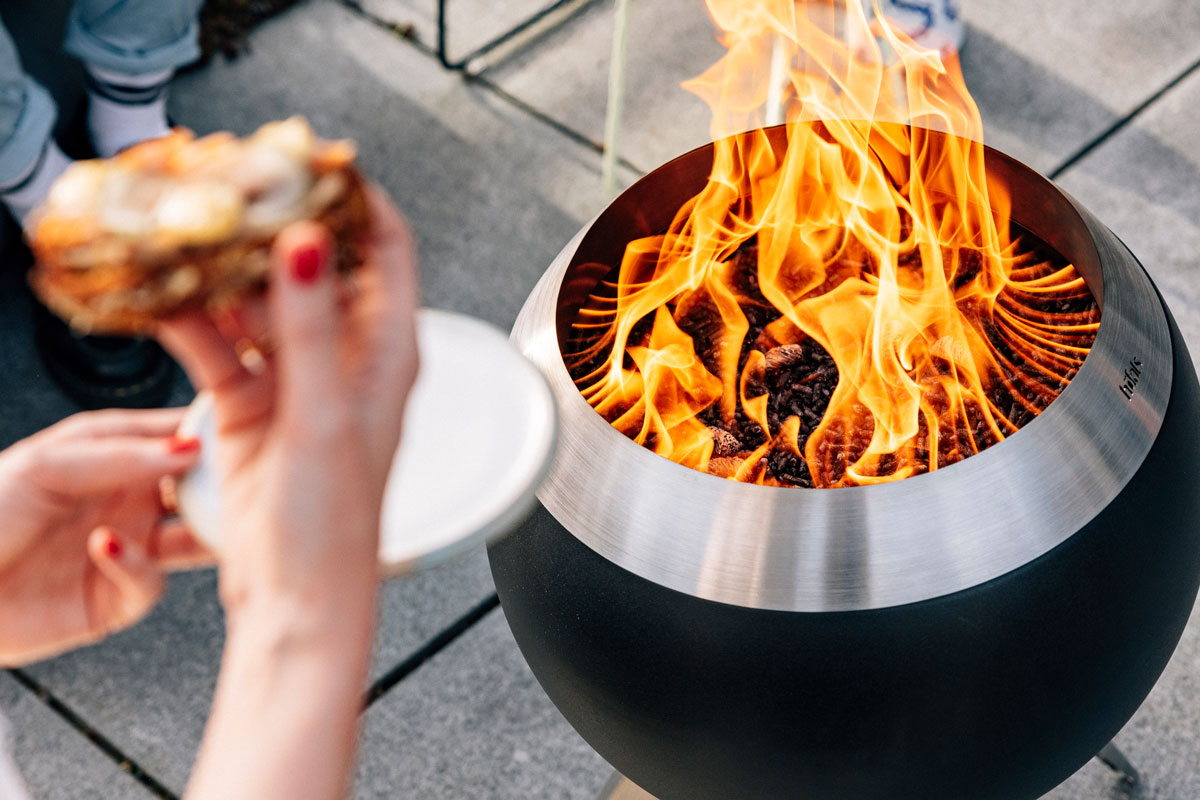 Premium Holzpellets 2x15kg Set Die 01003 Premium Holzpellets werden im Einsatz mit dem MOON 45 gezeigt, wo eine Person ein Stück Essen vor einem Feuergrube hält.