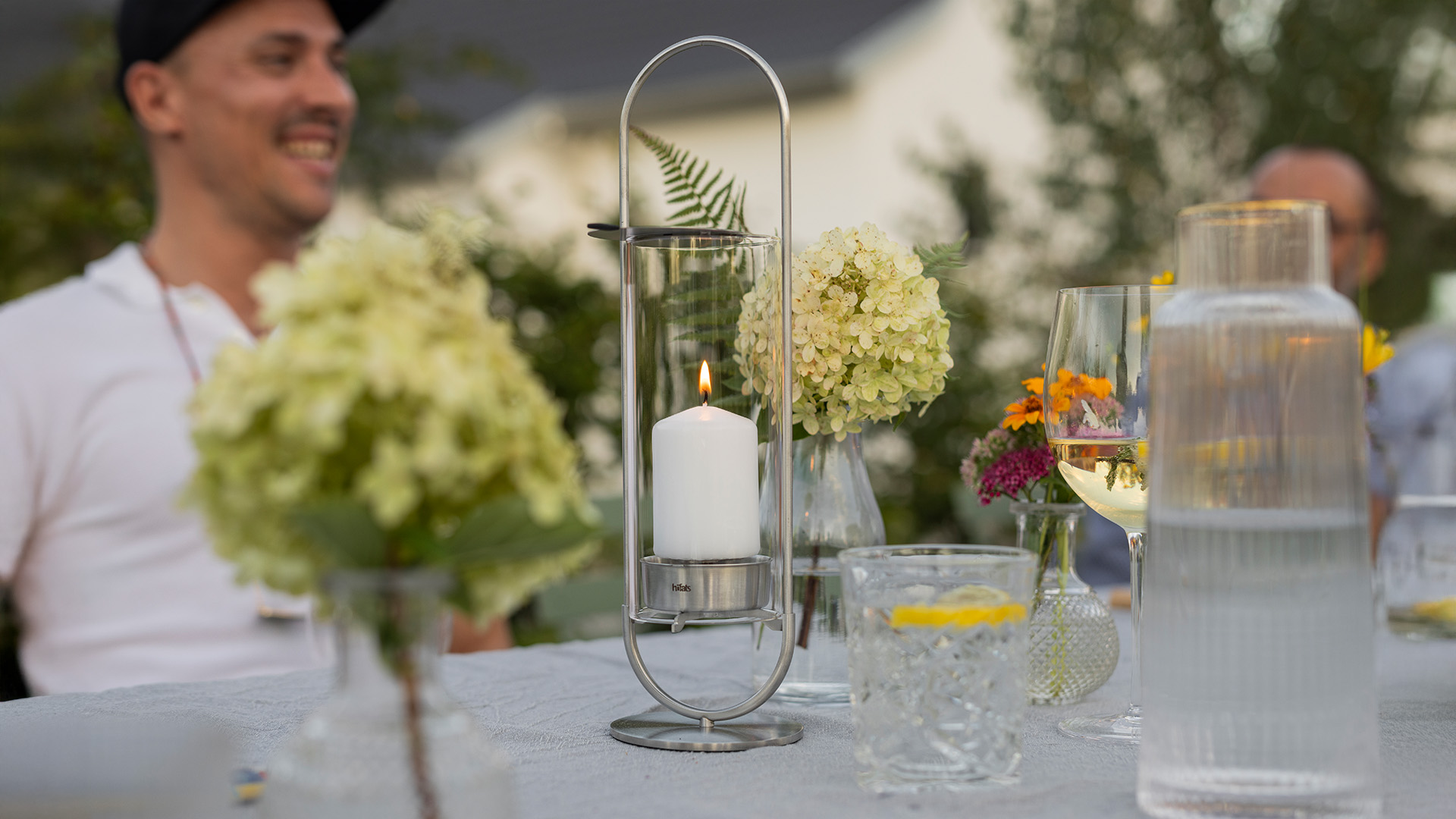 Ervaar een man die aan een tafel zit met bloemen en kaarsen met de verfijnde touch van de 00271 Ovale Kaars 35.