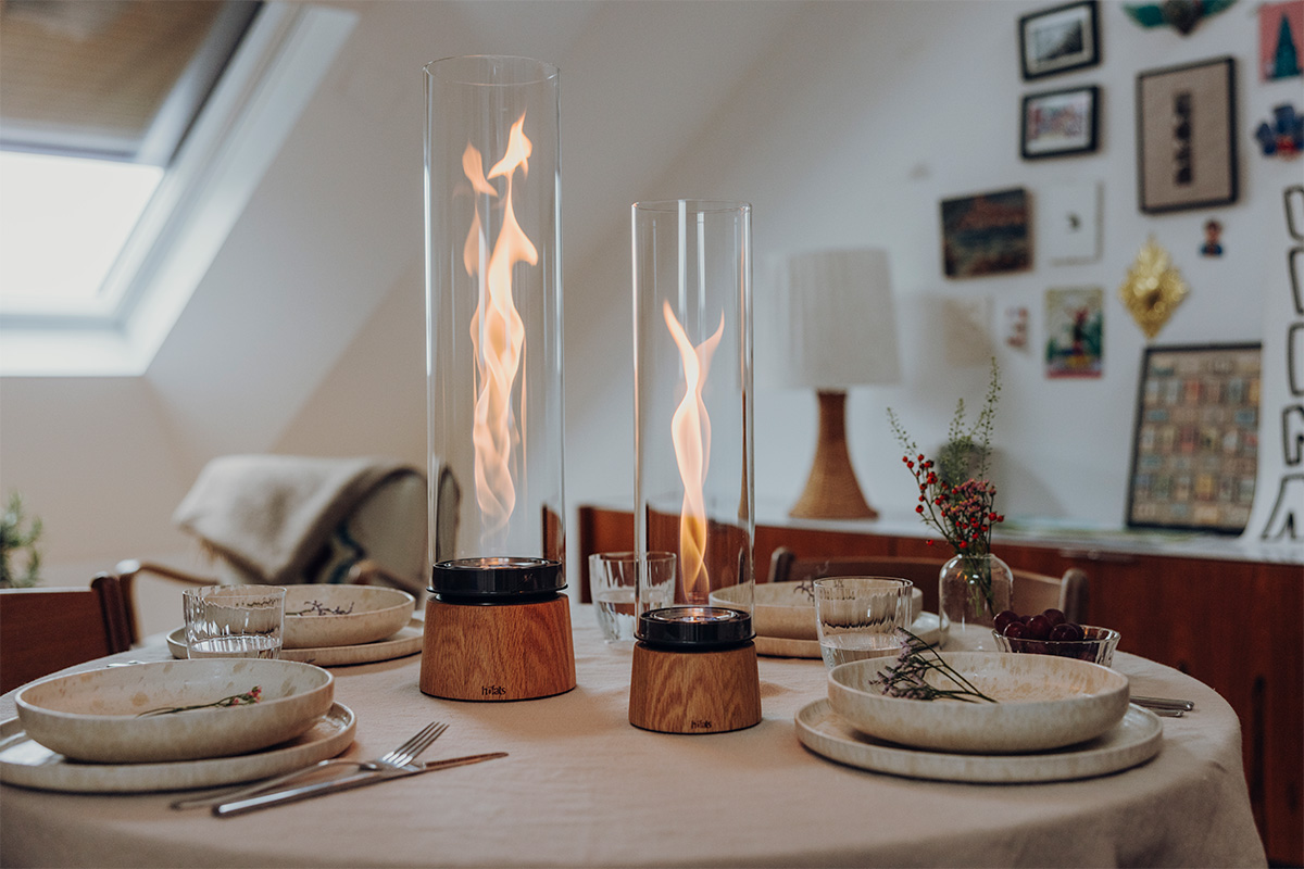 SPIN air 900 Tischfeuer Eiche SPIN air 1200 und 900 Tischfeuer Eiche natür stehen auf einem runden gedeckten Tisch im Hintergrund sind Bilder an der Wand