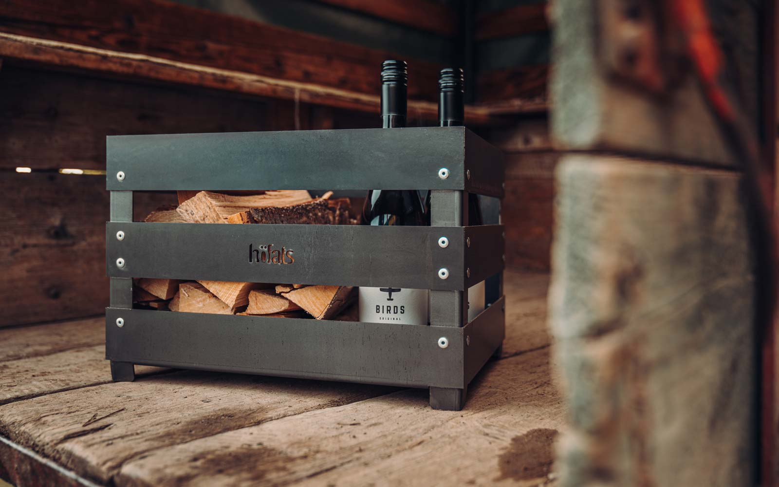 Eine Metallkiste mit einer Flasche Wein darin, bereichert durch die Anwesenheit des Crate Firebaskets, der Design mit Funktionalität vereint.