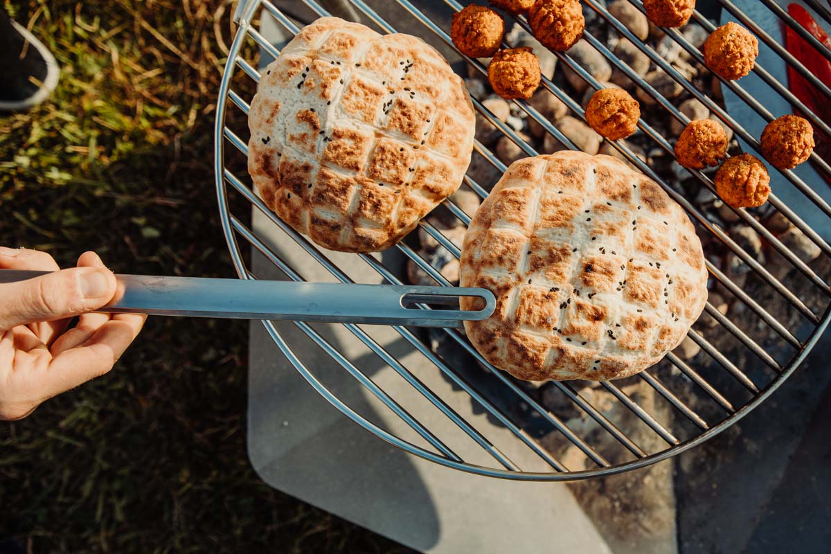 De Triple 90 Openhaard BBQ Set integreert naadloos in de omgeving, waar een persoon eten bereidt op een grill.