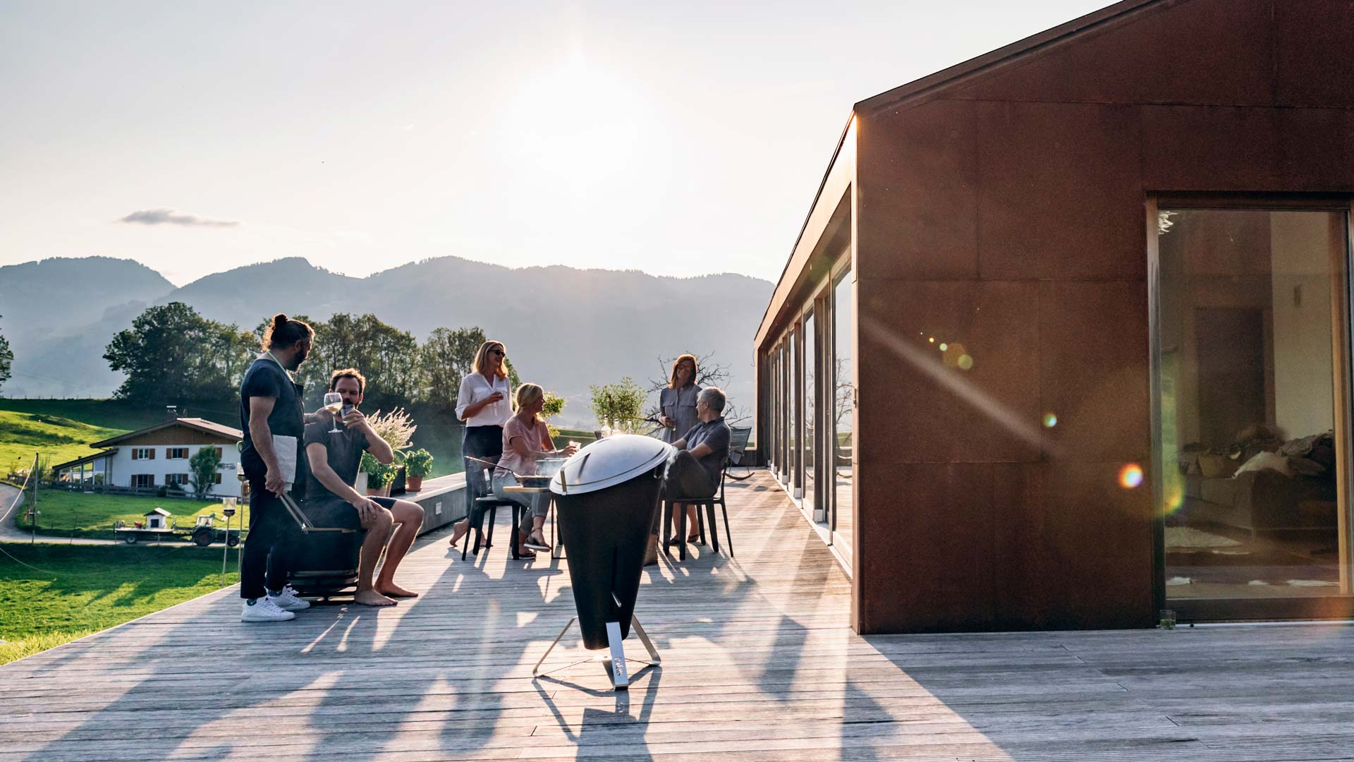 This image shows a group of people sitting on a wooden deck, with the CONE Charcoal Grill.