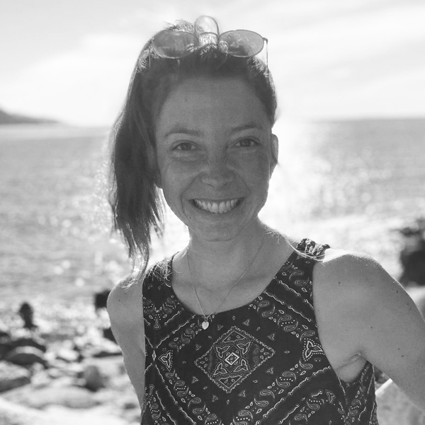 Eine Frau steht am Strand mit verschränkten Armen.