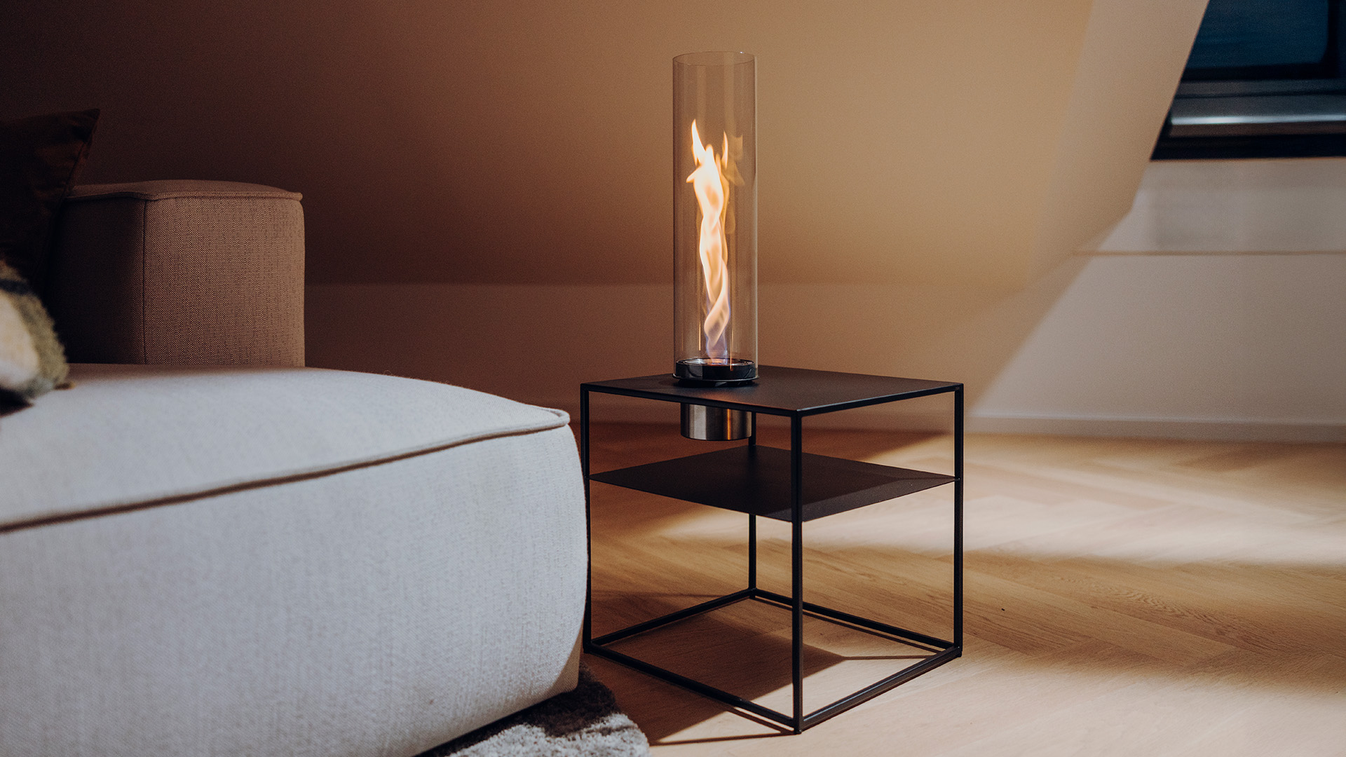 FIRE FRAME mit SPIN air 1200 Einbau steht mit lodernder Flamme im Wohnzimmer neben einer grauen Couch.