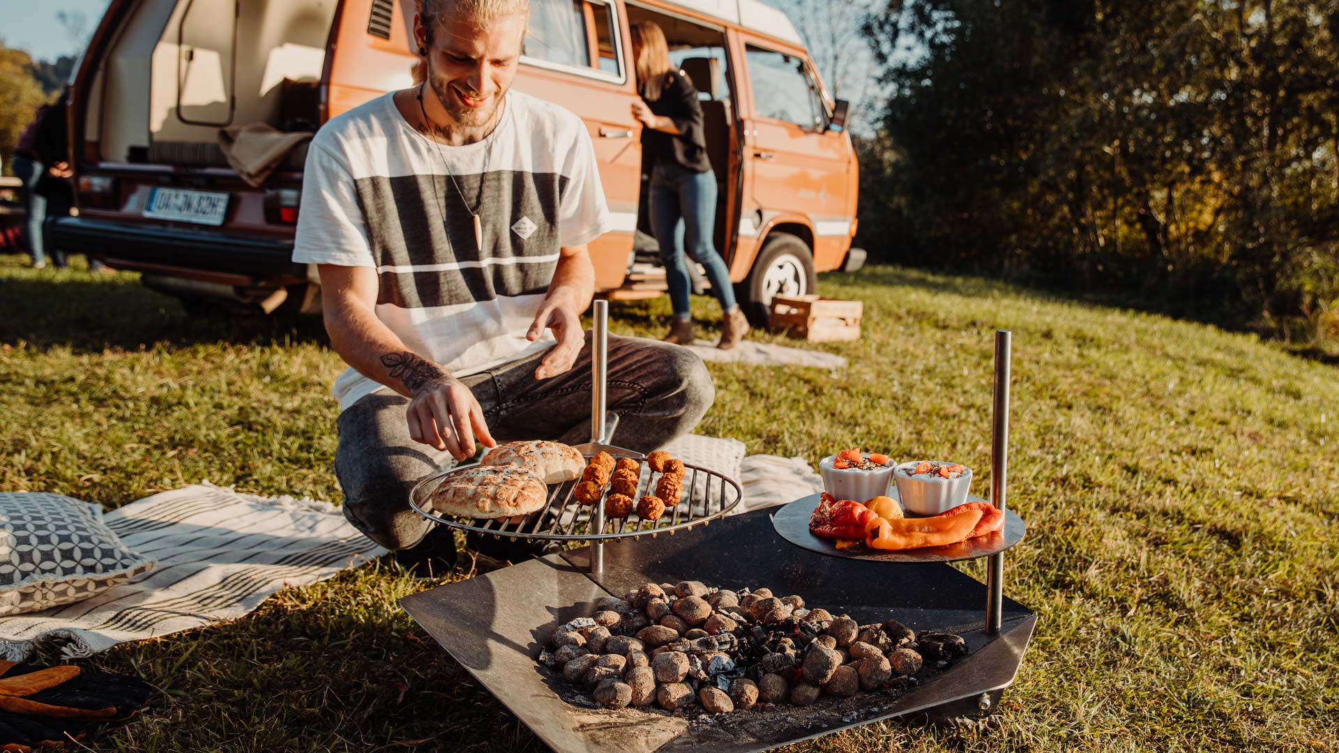 Der Triple 90 Kamin Multiset fügt sich nahtlos in die Umgebung ein, wo ein Mann auf dem Gras sitzt und grillt.