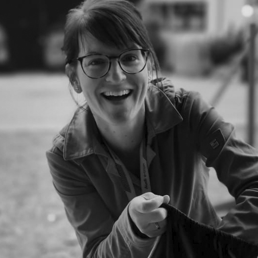 Eine Frau mit Brille lächelt und hält ein SkateBrett.